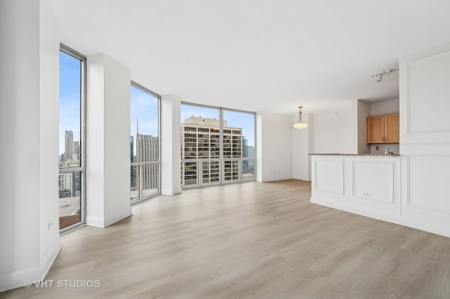 unfurnished living room featuring expansive windows, rail lighting, and light hardwood / wood-style floors