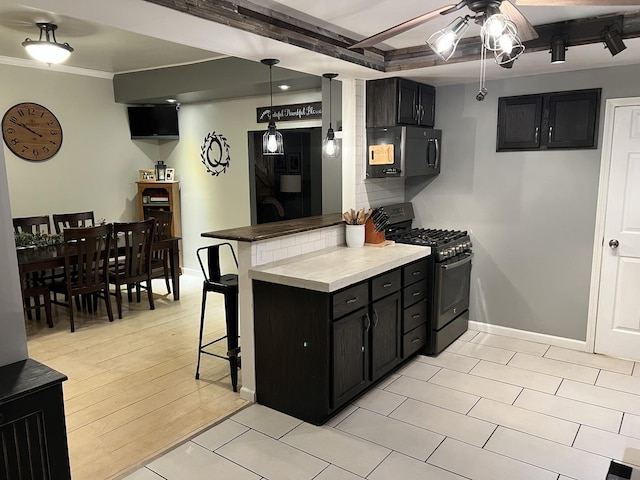 kitchen with a breakfast bar, stainless steel range with gas stovetop, ornamental molding, decorative backsplash, and kitchen peninsula