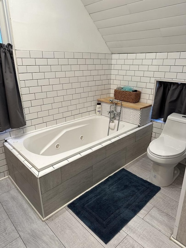 bathroom with toilet, lofted ceiling, and tiled bath