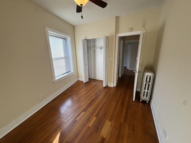 unfurnished bedroom featuring dark wood-type flooring, radiator heating unit, ceiling fan, and a closet