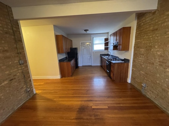 kitchen featuring dark wood-type flooring, brick wall, and black appliances