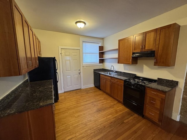 kitchen with sink, light hardwood / wood-style flooring, dark stone counters, and black appliances