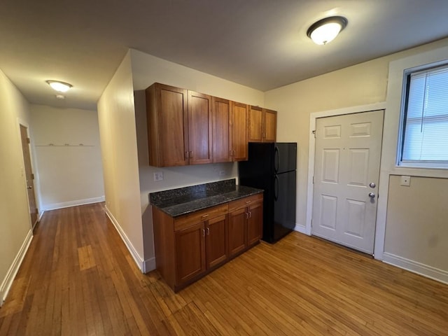 kitchen featuring black fridge, light hardwood / wood-style floors, and dark stone countertops