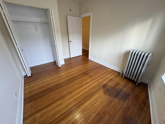 unfurnished bedroom featuring dark hardwood / wood-style flooring, radiator heating unit, and a closet