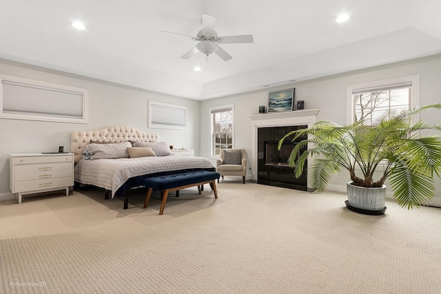 bedroom featuring light carpet, a fireplace, a raised ceiling, and ceiling fan