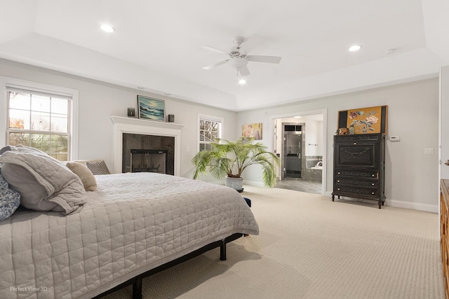 carpeted bedroom featuring a raised ceiling, ceiling fan, a high end fireplace, and multiple windows