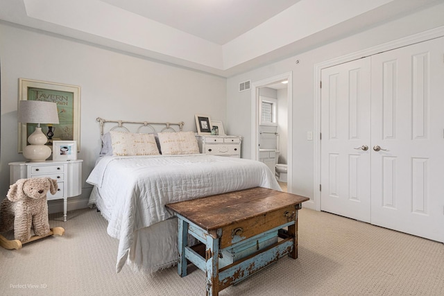 bedroom featuring light colored carpet, ensuite bath, and a closet