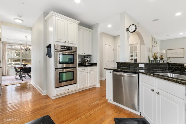 kitchen featuring sink, appliances with stainless steel finishes, white cabinetry, dark stone countertops, and light hardwood / wood-style floors