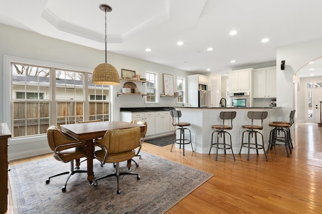 dining space featuring a raised ceiling, sink, and light wood-type flooring