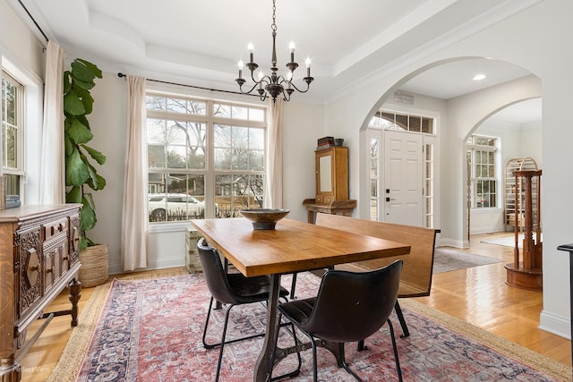 dining space featuring ornamental molding, a tray ceiling, a chandelier, and light hardwood / wood-style flooring