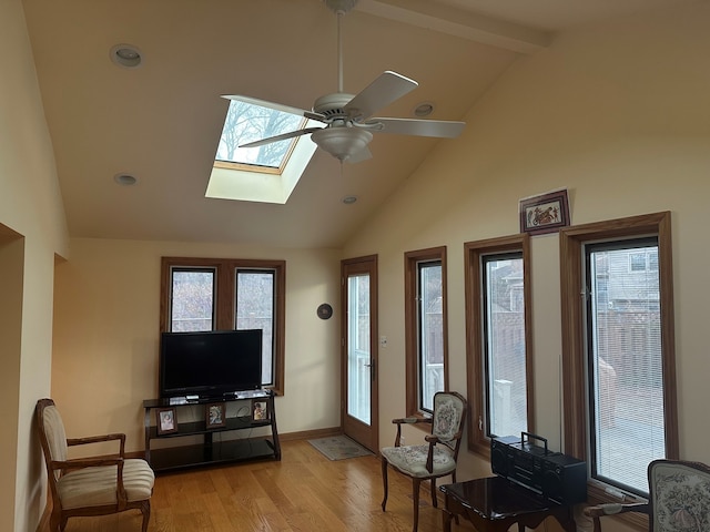 living room featuring a skylight, high vaulted ceiling, light wood-type flooring, beamed ceiling, and ceiling fan