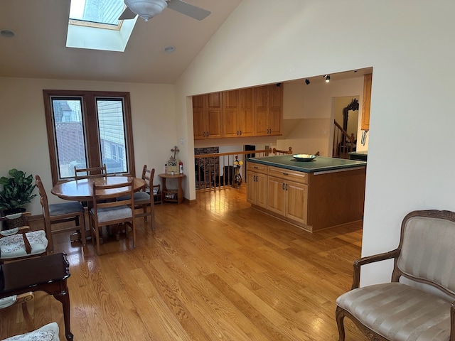 kitchen featuring ceiling fan, high vaulted ceiling, a skylight, and light hardwood / wood-style floors