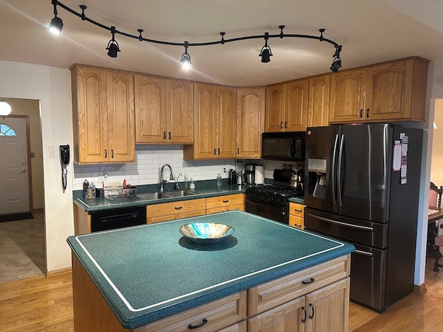 kitchen with sink, tasteful backsplash, black appliances, a kitchen island, and light wood-type flooring