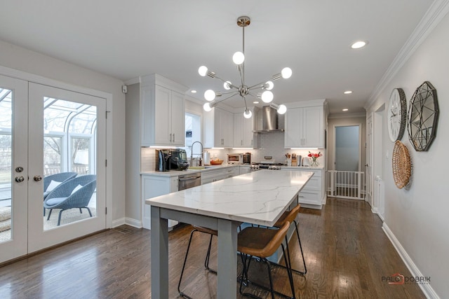 kitchen with decorative light fixtures, white cabinets, a center island, light stone counters, and wall chimney exhaust hood