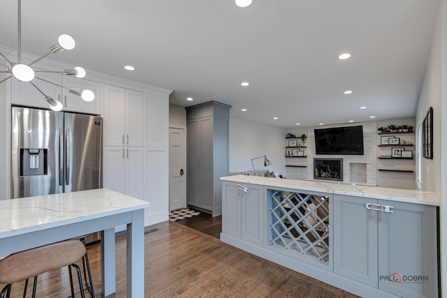 kitchen featuring white cabinets, stainless steel fridge, dark hardwood / wood-style flooring, hanging light fixtures, and light stone countertops