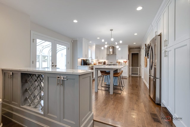 kitchen with stainless steel refrigerator, decorative light fixtures, white cabinetry, a breakfast bar area, and a center island