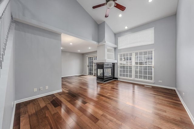 unfurnished living room with wood-type flooring, high vaulted ceiling, ceiling fan, and a multi sided fireplace