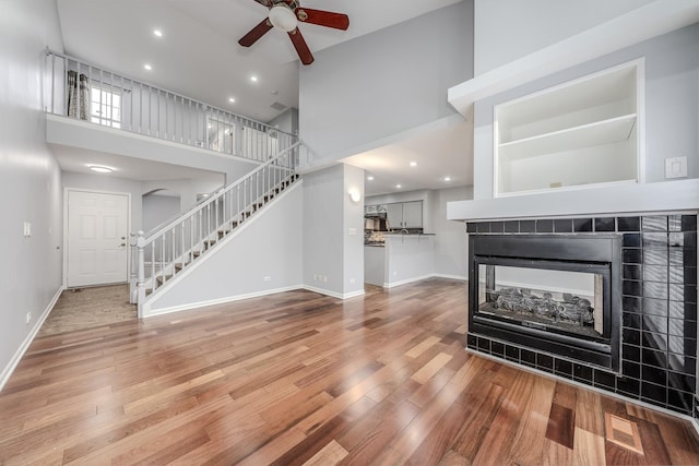 unfurnished living room with a tiled fireplace, a towering ceiling, wood-type flooring, and ceiling fan