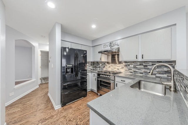 kitchen featuring sink, high end stainless steel range, light stone countertops, white cabinets, and black fridge with ice dispenser