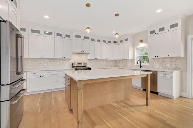 kitchen with white cabinetry, decorative light fixtures, a center island, light hardwood / wood-style flooring, and appliances with stainless steel finishes