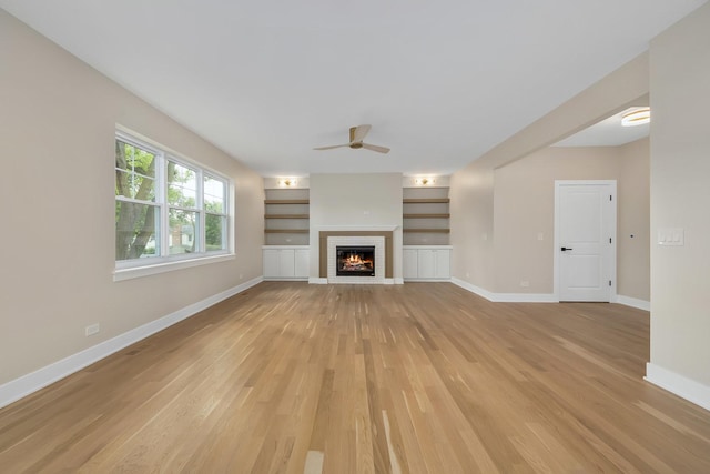 unfurnished living room featuring built in shelves, a fireplace, light hardwood / wood-style floors, and ceiling fan