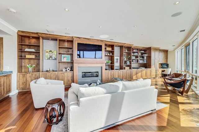 living area with visible vents, a glass covered fireplace, ornamental molding, wood finished floors, and recessed lighting