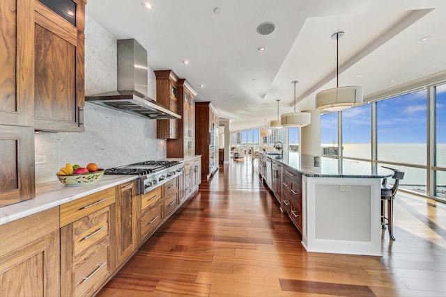 kitchen featuring stainless steel gas cooktop, dark wood-style flooring, wall chimney range hood, tasteful backsplash, and glass insert cabinets