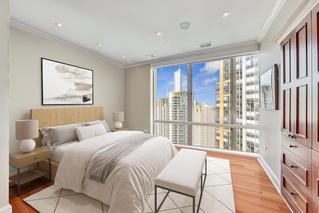 bedroom featuring light wood-type flooring, a view of city, crown molding, and recessed lighting