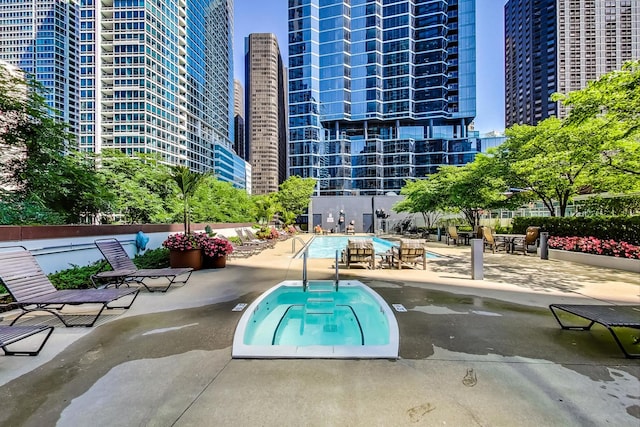 pool with a patio area, a hot tub, and a view of city