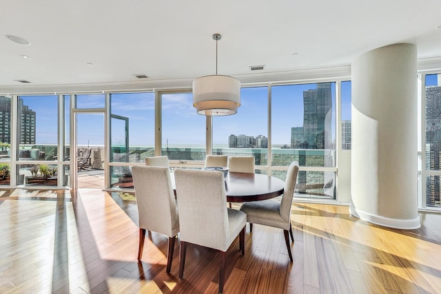 dining space featuring a view of city, floor to ceiling windows, visible vents, and hardwood / wood-style flooring