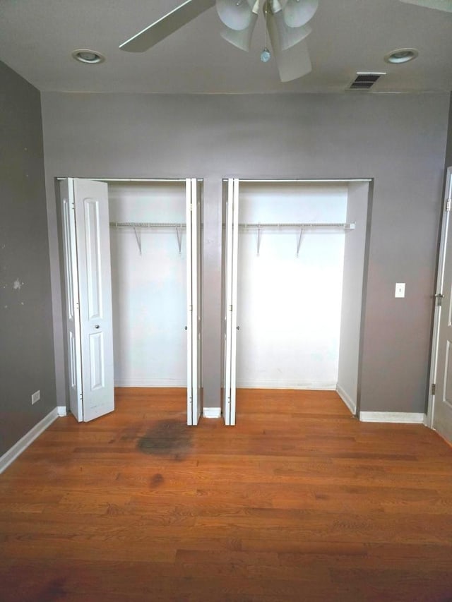 unfurnished bedroom featuring ceiling fan, two closets, and dark hardwood / wood-style flooring