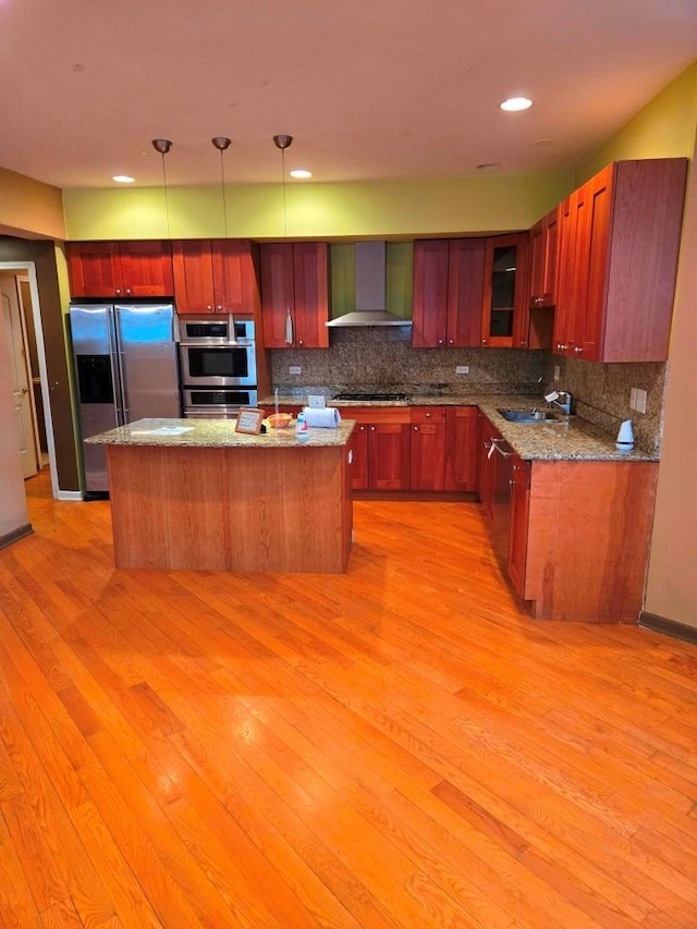 kitchen with a kitchen island, appliances with stainless steel finishes, decorative light fixtures, light stone countertops, and wall chimney exhaust hood