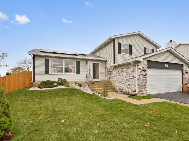 split level home with a garage, a front yard, and solar panels