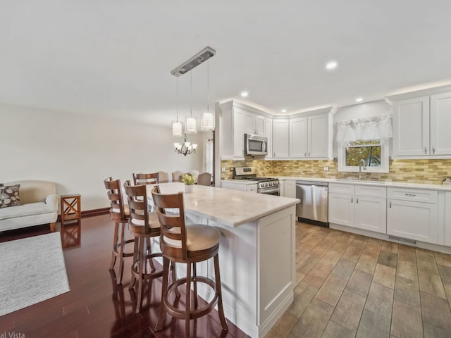 kitchen featuring a kitchen bar, sink, white cabinetry, hanging light fixtures, and stainless steel appliances