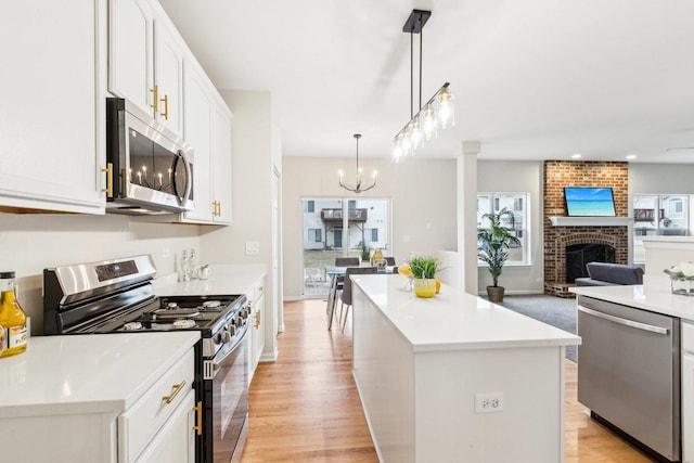 kitchen with white cabinetry, a brick fireplace, appliances with stainless steel finishes, a kitchen island, and pendant lighting