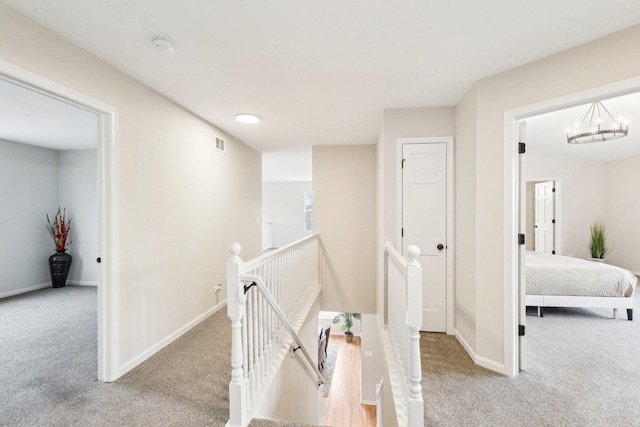 corridor with light colored carpet and a notable chandelier