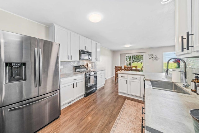 kitchen with tasteful backsplash, white cabinetry, sink, black appliances, and light wood-type flooring