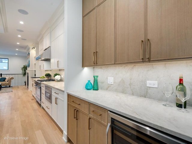 kitchen featuring high end stove, white cabinets, beverage cooler, light stone countertops, and light hardwood / wood-style flooring