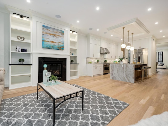 living room featuring built in shelves, crown molding, sink, and light wood-type flooring