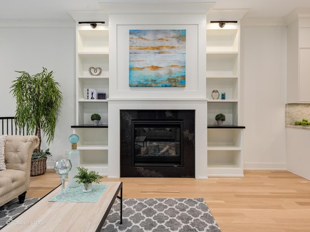 living room with built in shelves, ornamental molding, and light hardwood / wood-style flooring