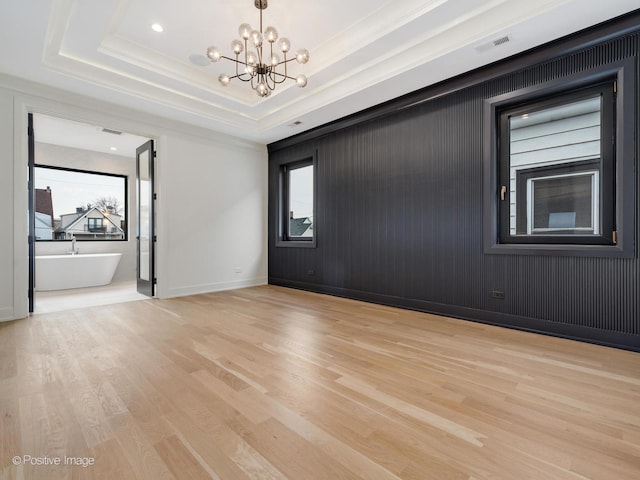 spare room featuring a healthy amount of sunlight, a tray ceiling, a chandelier, and light hardwood / wood-style floors