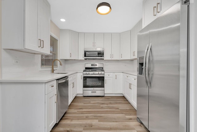 kitchen with appliances with stainless steel finishes, sink, white cabinets, and light hardwood / wood-style flooring