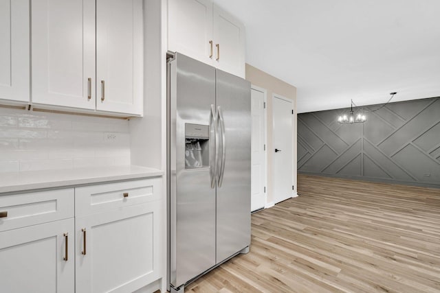 kitchen with white cabinetry, stainless steel fridge, hanging light fixtures, light hardwood / wood-style floors, and an inviting chandelier