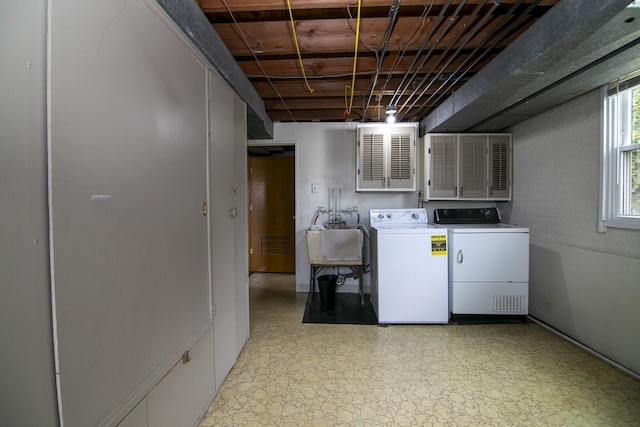 clothes washing area with washing machine and dryer, laundry area, a sink, light floors, and concrete block wall