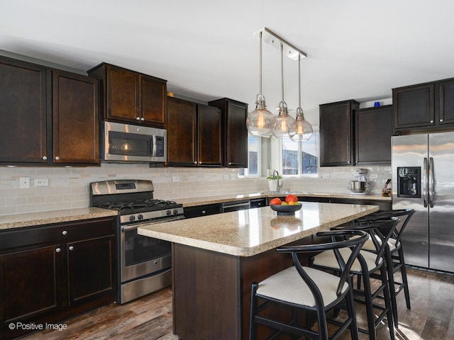 kitchen with dark wood-type flooring, appliances with stainless steel finishes, dark brown cabinetry, tasteful backsplash, and a kitchen island