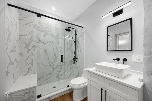 bathroom with a marble finish shower, vanity, toilet, and wood finished floors