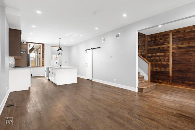 unfurnished living room featuring recessed lighting, a barn door, dark wood-type flooring, baseboards, and stairs