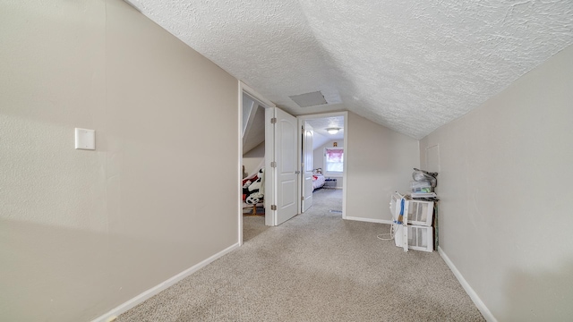 hallway with lofted ceiling, light colored carpet, and a textured ceiling