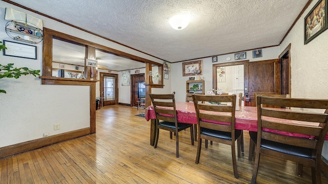 dining space featuring ornamental molding, light hardwood / wood-style floors, and a textured ceiling