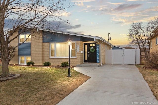 view of front of property featuring brick siding, concrete driveway, a front yard, and a gate